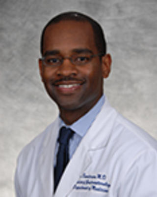 Andrew Sandersand is a bald man with glasses wearing a white coat, blue shirt, and blue tie.