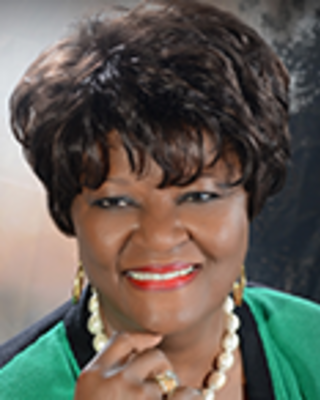 Shirley Marks has short black hair and is wearing a green blouse with a beaded necklace.