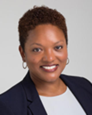 Michelle Taylor has short black hair. She is wearing a white shirt and black blazer.