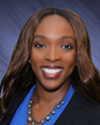 Shelly Taylor has long straight brown hair. She is wearing a blue blouse, beaded necklace, and black blazer.