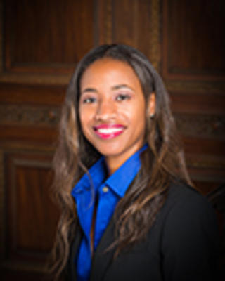 Deonza Thymes has long wavy brown hair. She is wearing a blue shirt and black blazer.