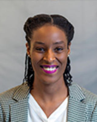 Trenika Williams has braided hair tied back and is wearing a white blouse with a patterned blazer.