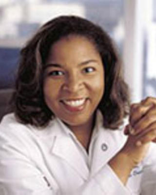 Valerae Lewis has medium-length black hair and is wearing a white coat.