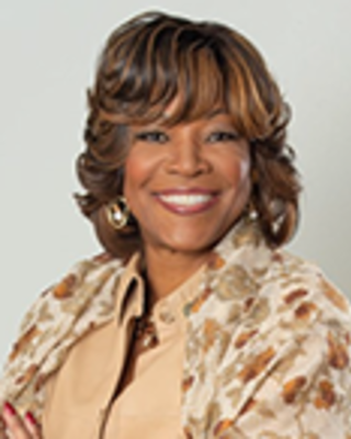 Valerie Montgomery-Rice has medium length brown hair and is wearing a beige printed blouse.