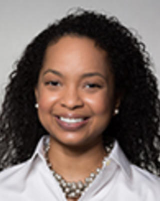 Shanele Williams has long curly black hair. She is wearing a white shirt and necklace.