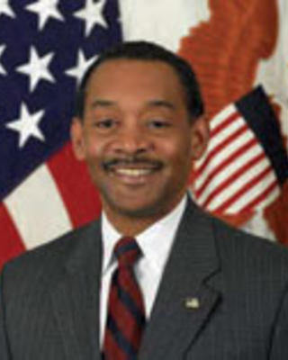 Jonathan Woodson has short black hair and is wearing a suit. He is in front of an American flag.