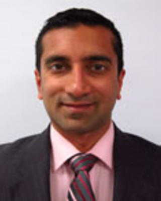 Jay Bhatt has short black hair. He is wearing a pink shirt, pink patterned tie, and black blazer.