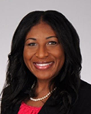 Brittany Watson has medium-length black hair. She is wearing a pearl necklace, red blouse, and black blazer.