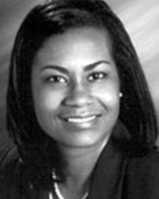 Laura Gerald has medium straight black hair. She is wearing a necklace, white blouse, and black blazer.