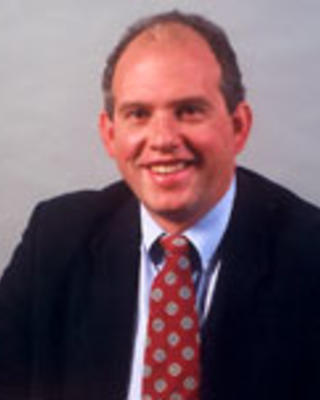 David Gifford has short dark hair and is wearing a suit with a printed red tie.