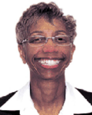 Joan Griffit has short brown hair and glasses. She is wearing a white shirt and black jacket.