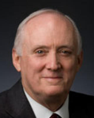 John Howe has short white hair and is wearing a suit.