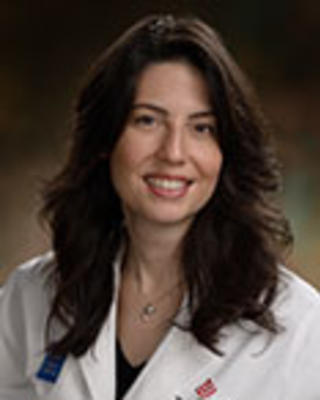 Keila Lopex has long wavy brown hair and is wearing a white coat.