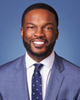 Kevin Simon has short black hair and facial hair. He is wearing a blue suit.
