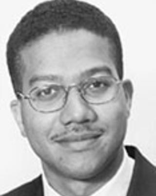 Roderick King has short black hair and glasses. He is wearing a suit.