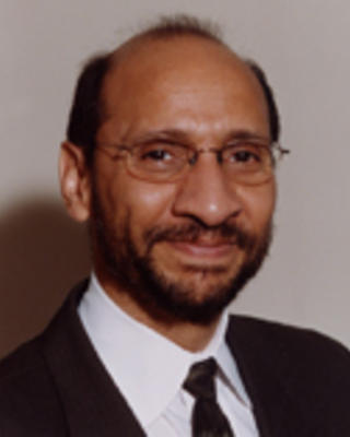 John Lumpkin has short black hair and glasses. He is wearing a suit.