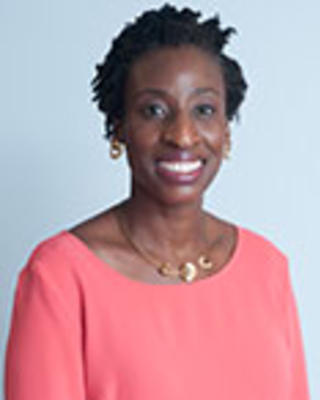 Salewa Oseni has short coily black hair. She is wearing a pink blouse and gold jewelry..