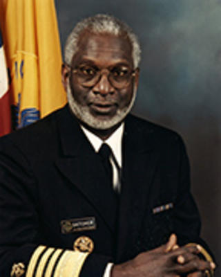 David Satcher has short gray hair and facial hair. He is wearing a Surgeon General uniform with his hands clasped in front of him.
