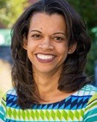 Shairi Turne has medium-length black hair. She is outside and wearing a green and blue patterned blouse.