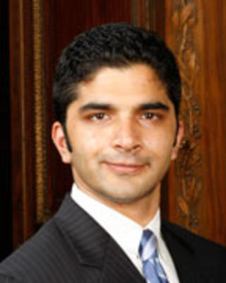 Sanjeev Sriram has short black hair and is wearing a suit.
