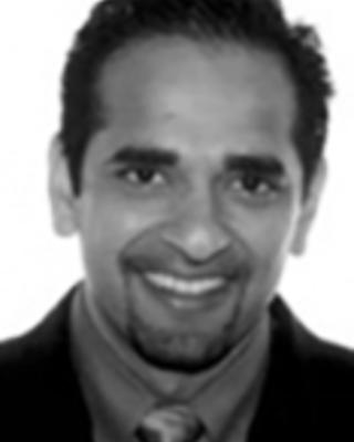 Amal Trivedi has short black hair and a goatee. He is wearing a suit.