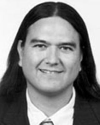 Donald Warne has long straight black hair. He is wearing a suit.