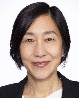 Alice Chen has short black hair. She is wearing a white blouse and black blazer.