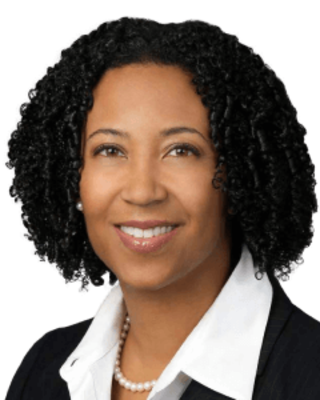 Dora Hughes is wearing a black blazer and white shirt. She has chin-length curly black hair.