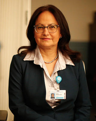 Nawal Nour has medium length black hair. She is wearing a black blazer, white shirt, and MGB nametag.