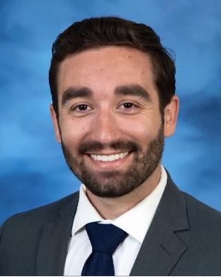Michael Harding has short black hair and facial hair. He is wearing a suit.