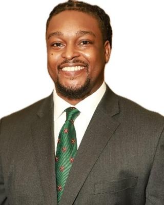 Matthew Moore has black hair and facial hair. He is wearing a suit.
