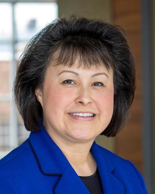 Yvette Roubideaux has short black hair with bangs. She is wearing a blue blazer and black top.