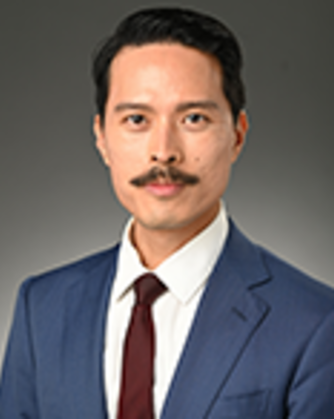 Jacques Ambrose has short black hair and a moustache. He is wearing a suit.