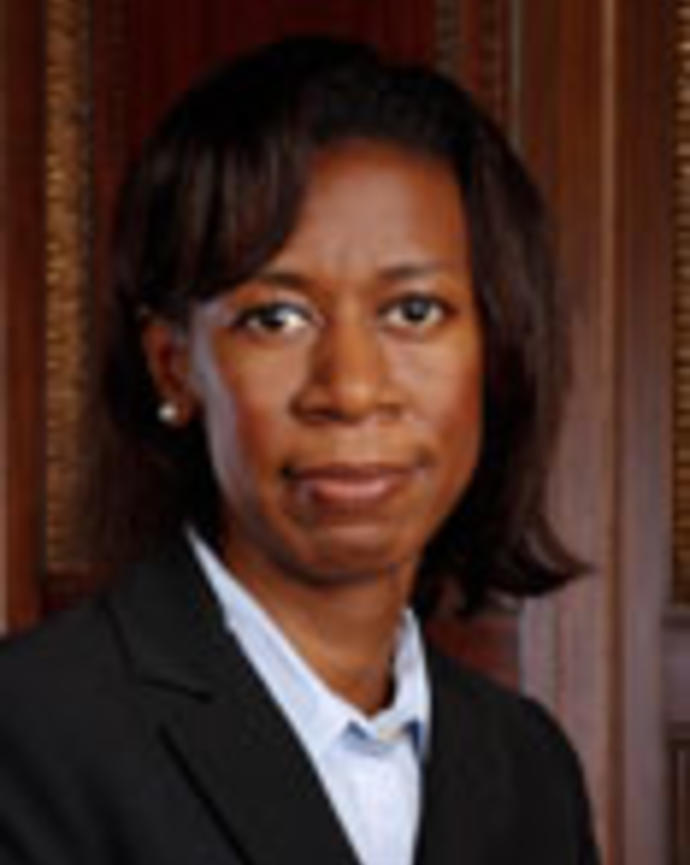 Ashaunta Tumblin has chin-length straight black hair. She is wearing a white shirt and black blazer.