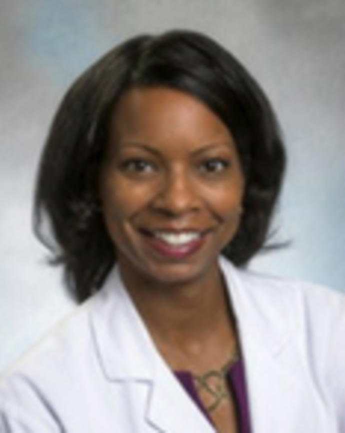 Audra Meadows has medium-length black hair and is wearing a white coat.