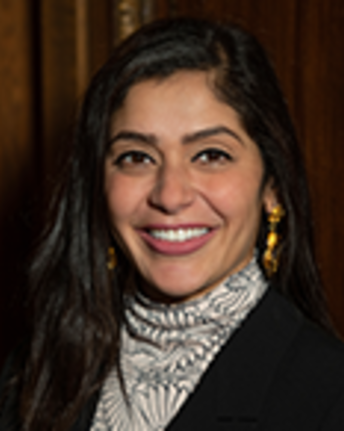 Nasrien Ibrahim has long black hair. She is wearing a printed turtleneck and black blazer.
