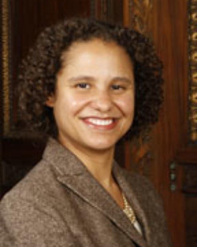 Julea McGhee has short curly brown hair and is wearing a brown blazer.