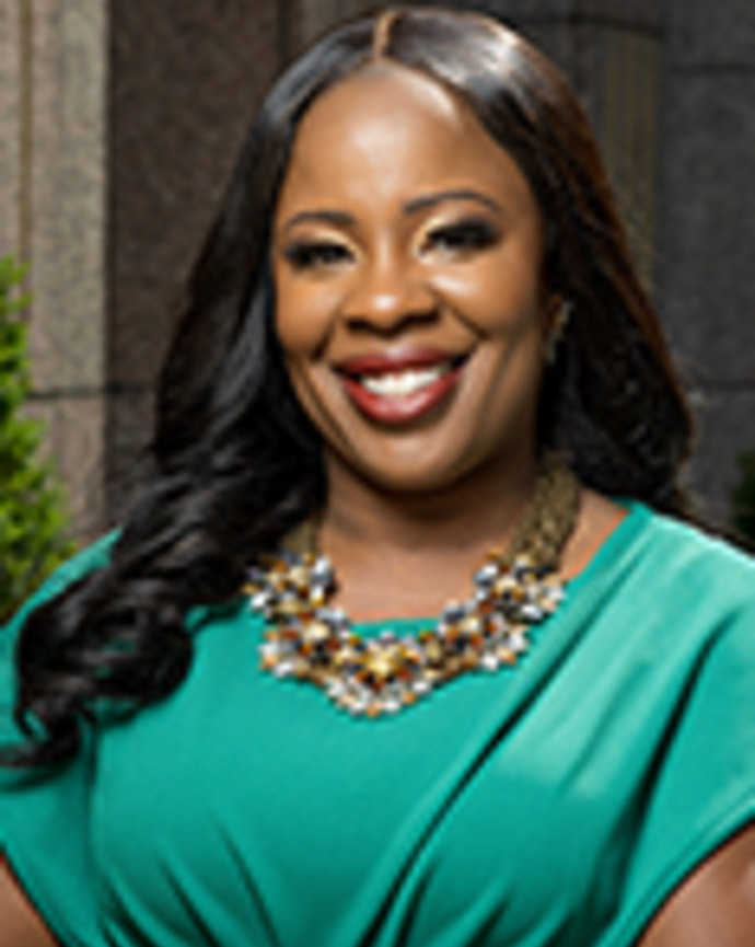 Nwando Olayiwola has long straight black hair. She is wearing a beaded necklace and green dress.