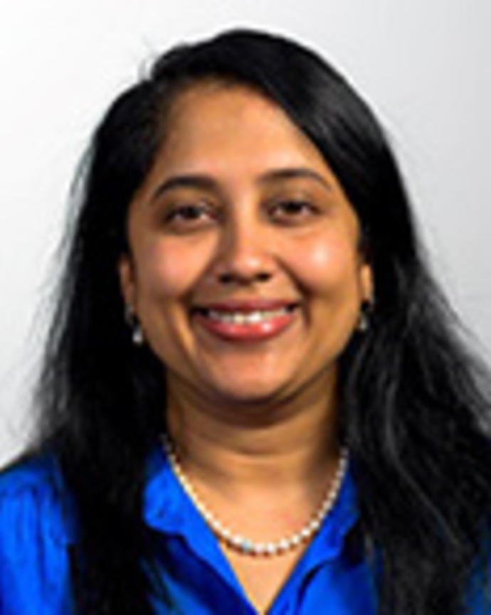 Preeta Chidambaran has long straight black hair and is wearing a blue shirt with a pearl necklace.