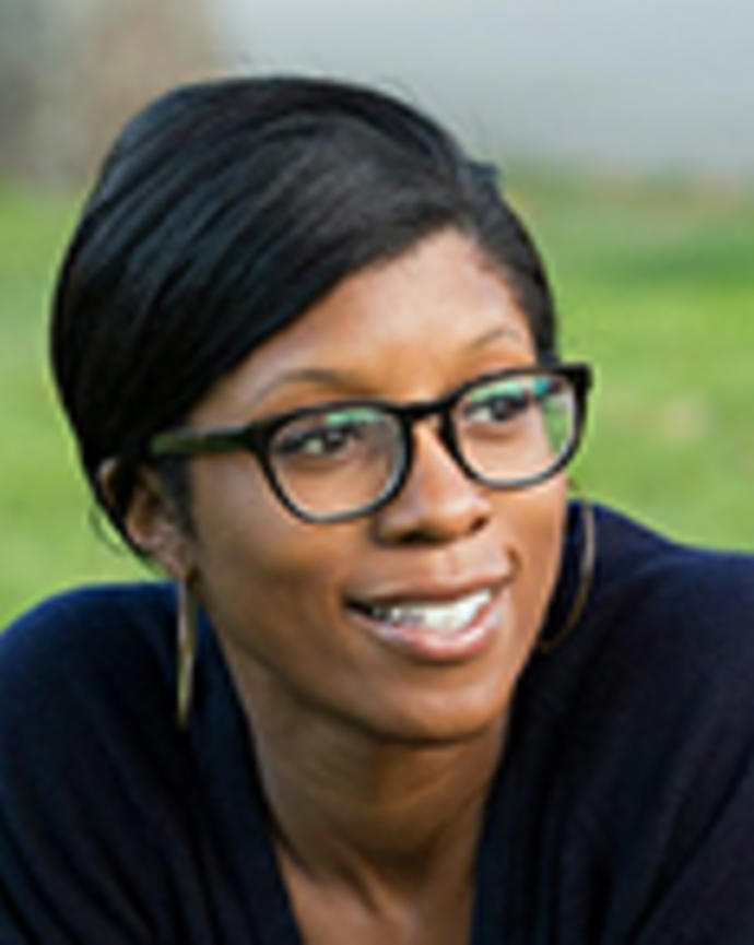 Rhea Boyd has short black hair and glasses. She is outside and looking to the side.