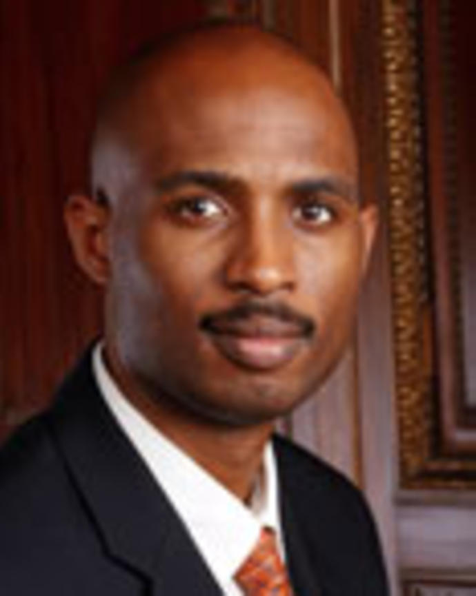 Roy Wade is a bald man with a moustashe. He is wearing a suit.