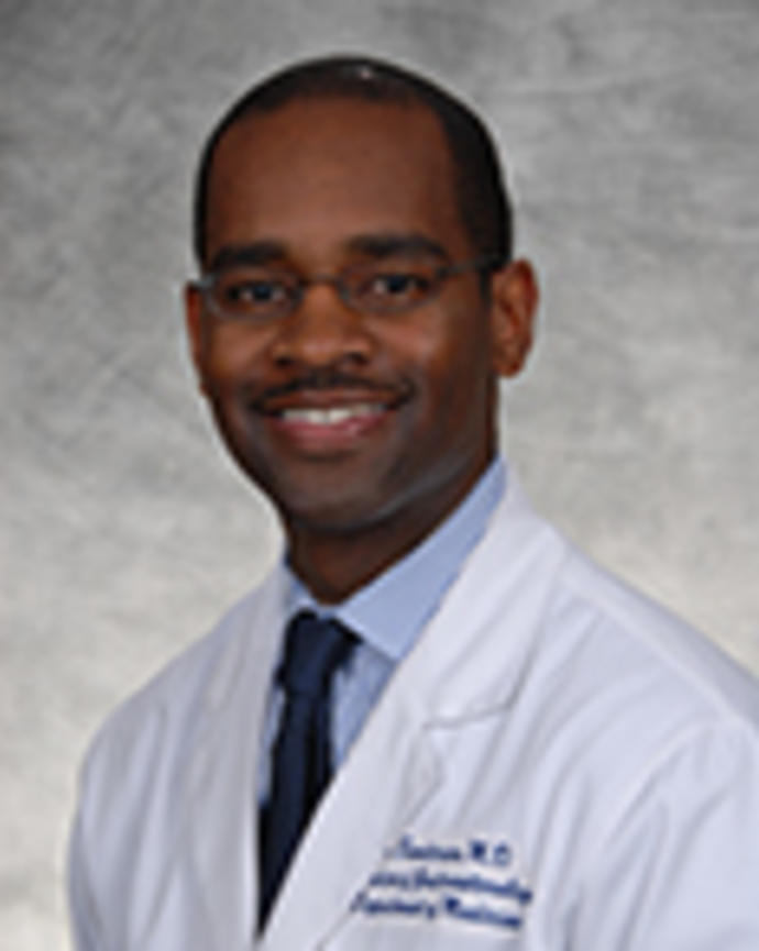 Andrew Sandersand is a bald man with glasses wearing a white coat, blue shirt, and blue tie.
