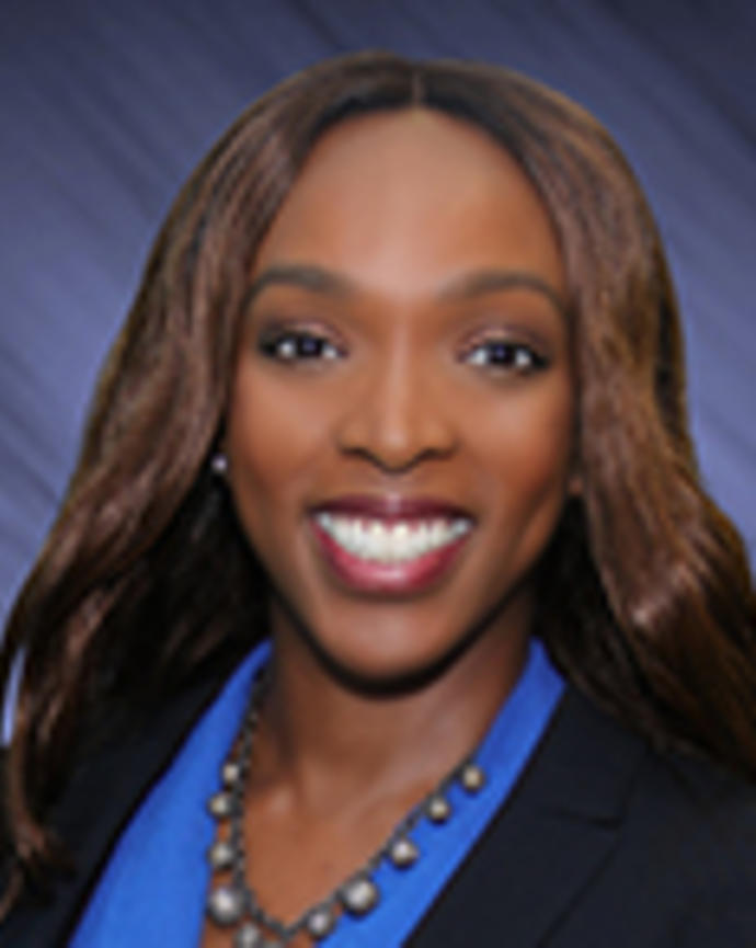 Shelly Taylor has long straight brown hair. She is wearing a blue blouse, beaded necklace, and black blazer.