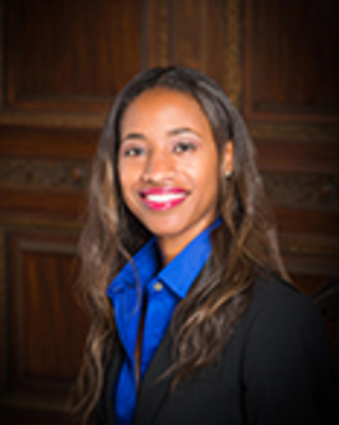 Deonza Thymes has long wavy brown hair. She is wearing a blue shirt and black blazer.