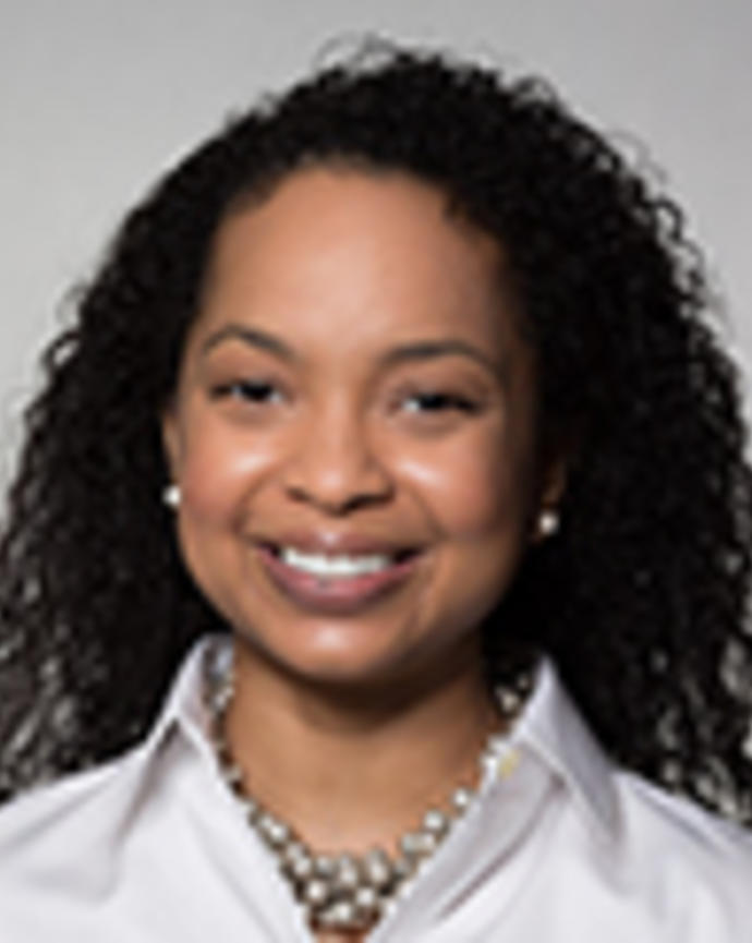 Shanele Williams has long curly black hair. She is wearing a white shirt and necklace.