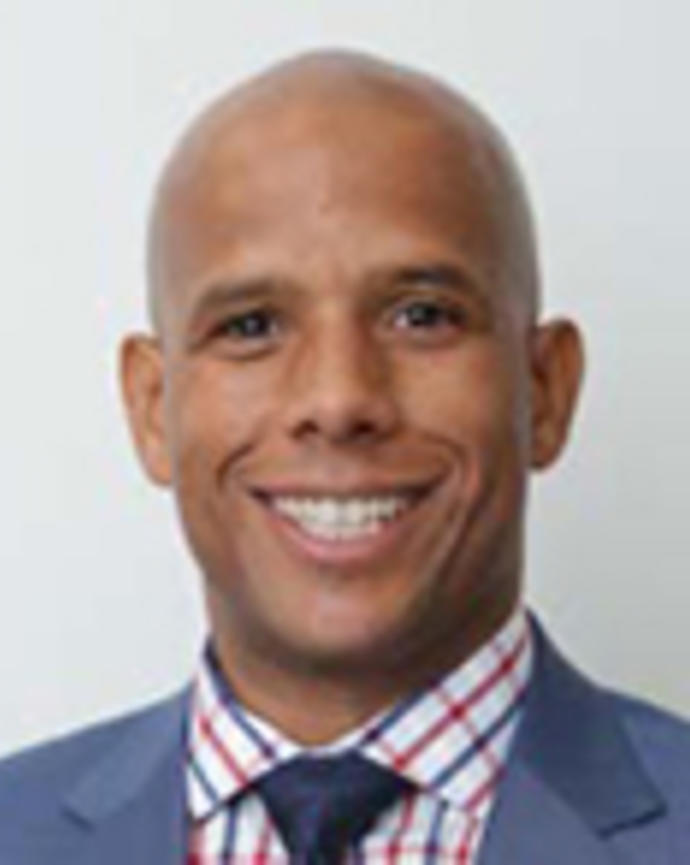 Alden Landry is a bald man wearing a printed shirt, dark blue tie, and blue blazer.