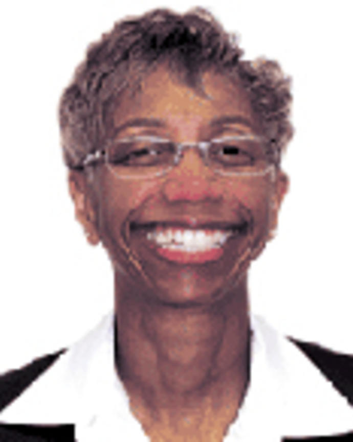 Joan Griffit has short brown hair and glasses. She is wearing a white shirt and black jacket.