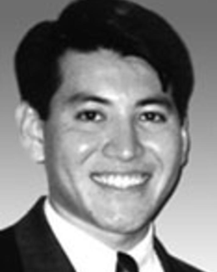 Arthur Hayashi has short black hair and is wearing a suit. 
