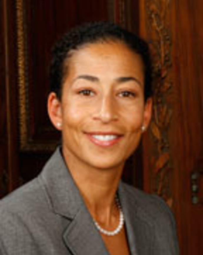 Samantha Kaplan has dark hair pulled back. She is wearing a gray blazer and pearl necklace.