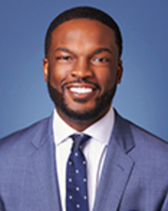 Kevin Simon has short black hair and facial hair. He is wearing a blue suit.